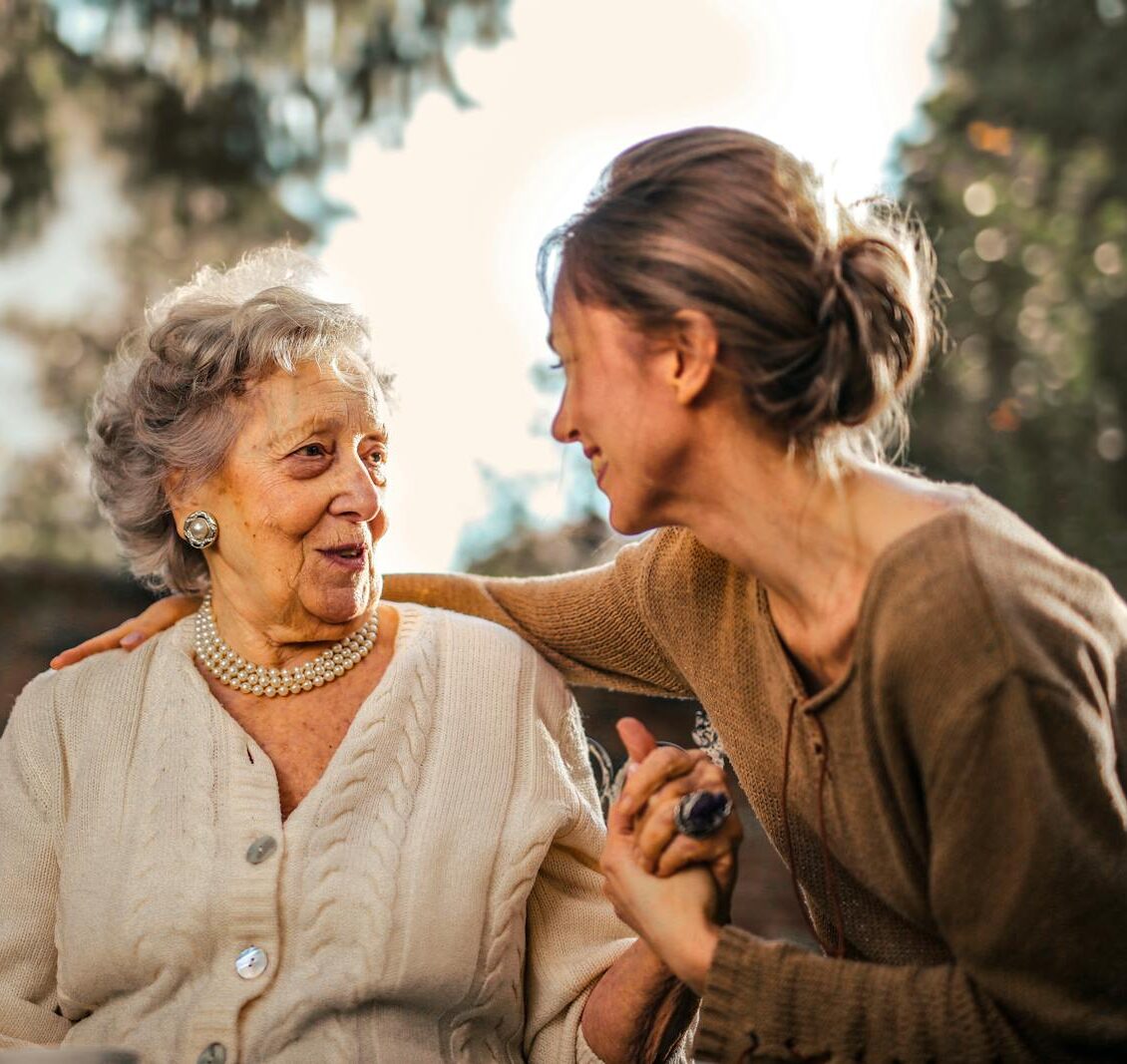 Elderly woman and adult daughter share a joyful, affectionate moment in a sunny garden.